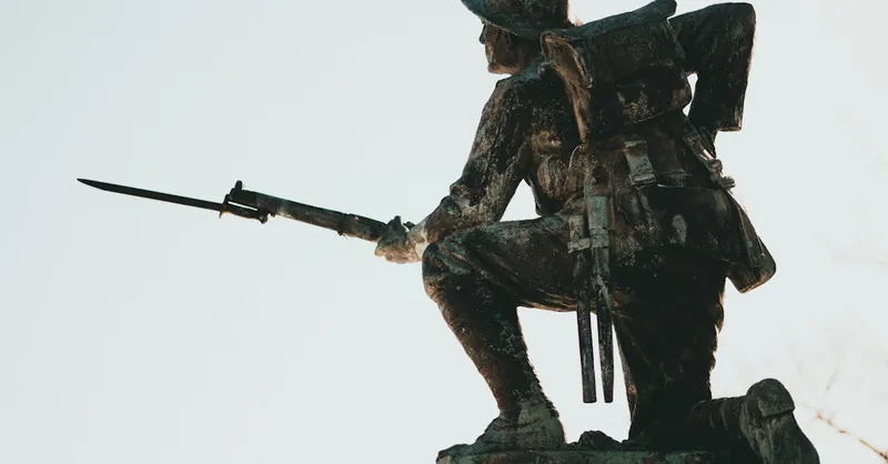 Bronze soldier statue with bayonet, symbolizing military history and valor in sunlight.