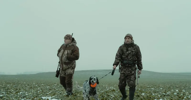 Hunters in camouflage with a dog in winter field, showcasing outdoor adventure and companionship.