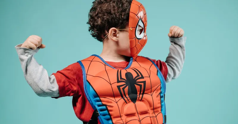 Young child posing in Spider-Man costume with turquoise background showcasing imagination.
