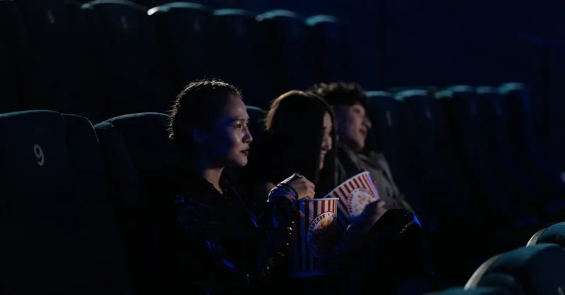 Group of friends watching a movie in a dark cinema, enjoying popcorn.