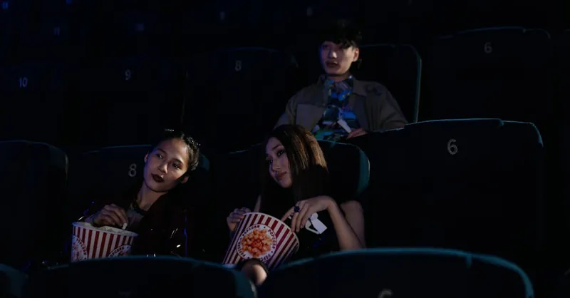 A group of friends enjoying a movie in a dimly lit theater, holding popcorn.