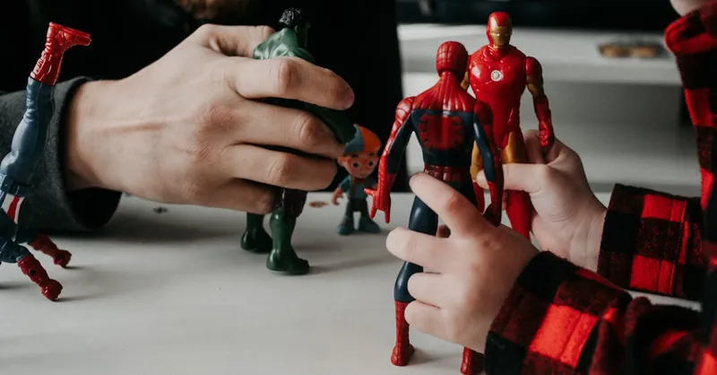 A father and son bond while playing with superhero action figures indoors.