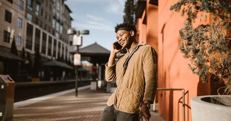 Smiling young man in a city setting talking on his phone outdoors.