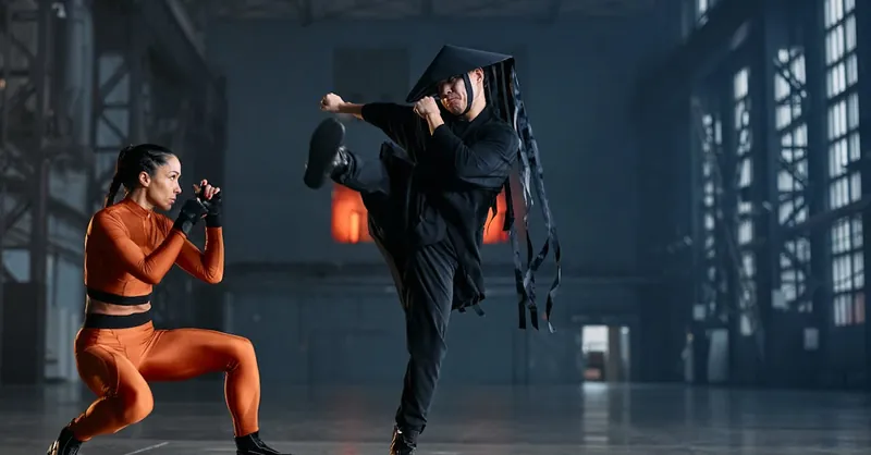 Two cosplayers performing martial arts poses in an industrial space, showcasing vibrant costumes and action.