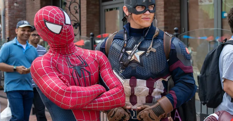 Spider-Man and Captain America cosplayers pose in a lively street scene with onlookers.