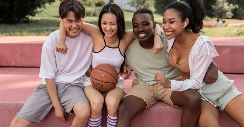 A diverse group of young friends sharing joyful moments outdoors with a basketball.