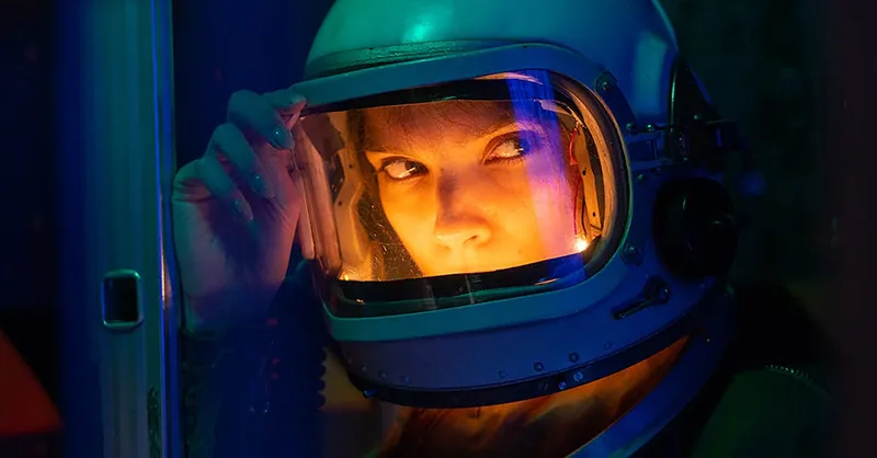 Portrait of a spacewoman in a helmet gazing intensely with colorful lighting.
