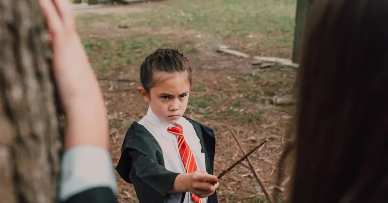 A child dressed as a wizard holding a wand outdoors, embodying fantasy and magic.