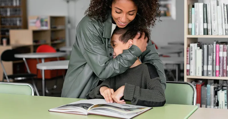 A caring teacher embraces a student in a library, fostering a warm and supportive learning environment.