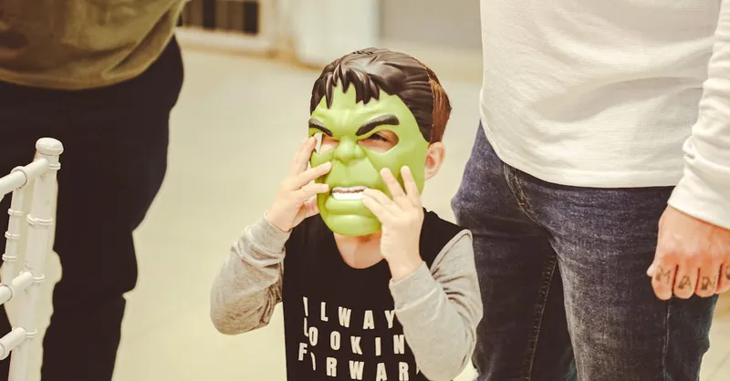 Young boy in Hulk mask standing with adults indoors, embodying superhero fun.