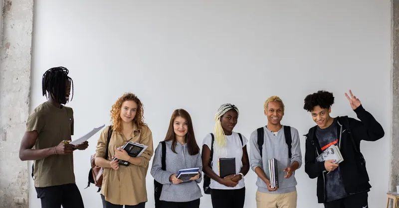 A group of cheerful, diverse college students posing together with books indoors.